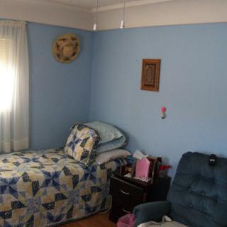 A small bedroom with a single bed and blue walls, featuring an armchair and a nightstand.