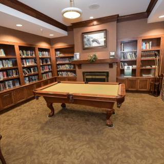 A cozy library interior featuring bookshelves, a fireplace, and a billiards table.