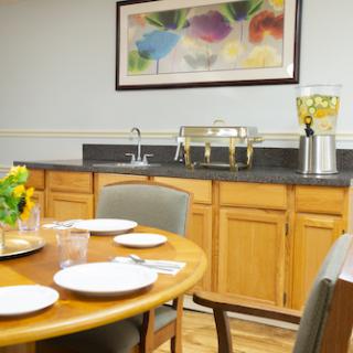 A cozy dining area featuring a wooden table set for a meal, accompanied by a beverage dispenser and decorative flowers.