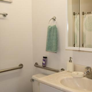 A bathroom with a sink, mirror, and handrails.