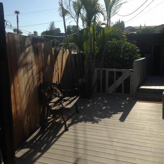 A sunny outdoor deck area with wooden chairs, a fence, and palm trees.