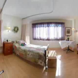 A cozy bedroom with a single bed, wooden flooring, and soft natural light filtering through the window curtains.