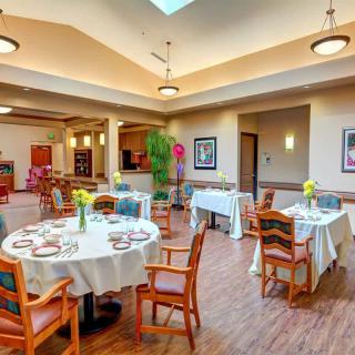 A well-lit dining room with neatly arranged tables and chairs, featuring floral decorations and modern decor.