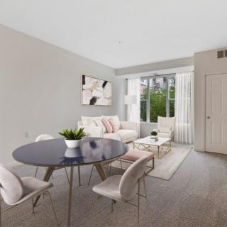 A modern living room with a dining area featuring neutral colors and minimalist design, enhanced by natural light and an indoor plant.