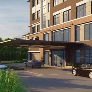 A modern building entrance with cars parked in the driveway.