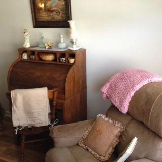 A cozy living room corner featuring a recliner with a pink throw, a wooden secretary desk adorned with decorative items, and a rocking chair.