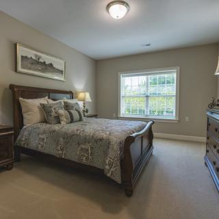 A cozy bedroom featuring a neatly made bed, wooden furniture, and natural light streaming through the window.