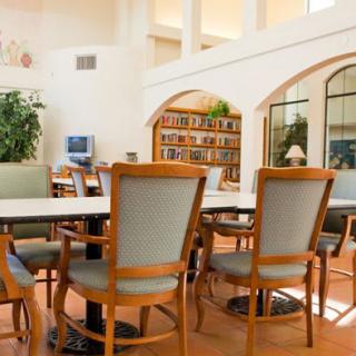 A bright library space with tables and chairs, surrounded by bookshelves and plants.