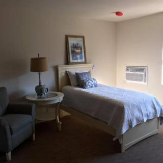 A cozy bedroom with a single bed, chair, and lamp.