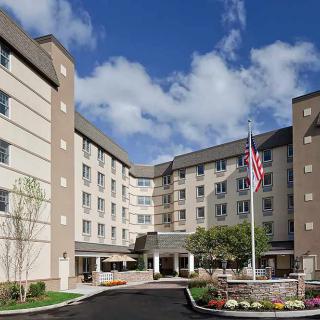 A modern hotel building with an American flag displayed at the entrance on a partly cloudy day.