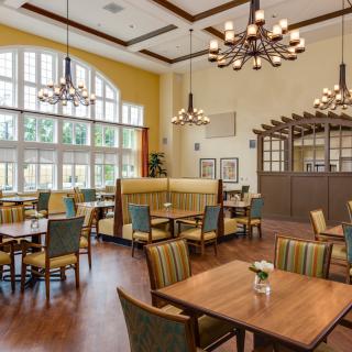 A well-lit dining area featuring wooden tables and chairs, elegant chandeliers, and large windows that allow natural light to fill the space.