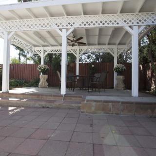 A backyard pergola providing shade over a patio area with furniture and decorative plants.