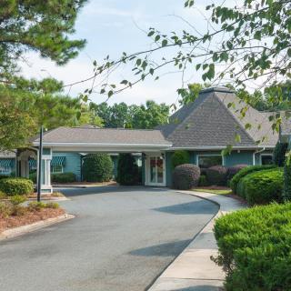 A quaint building with a circular driveway surrounded by trees and shrubs.