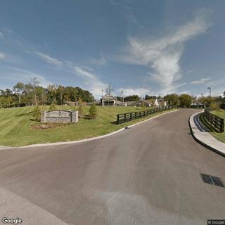 A road leading into a park with a visible sign and surrounding trees under a clear sky.