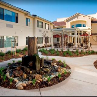 A courtyard featuring a central fountain surrounded by landscaping, adjacent to a large building with multiple floors.
