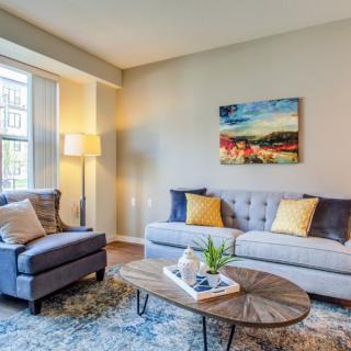 A cozy living room with modern decor, featuring a sofa, armchair, coffee table, and vibrant artwork.