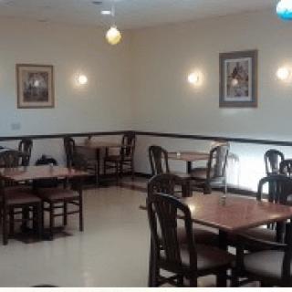 An empty restaurant dining area with tables and chairs arranged neatly under warm lighting.