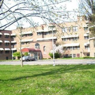 A residential apartment building with a well-maintained lawn and trees in the foreground.