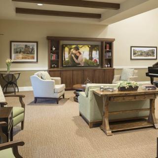 A cozy and elegant living room with comfortable seating, a TV on a wooden cabinet, decorative artwork, and a piano.