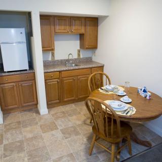 A small kitchen and dining area with wooden cabinets, a refrigerator, and a round table set for two.