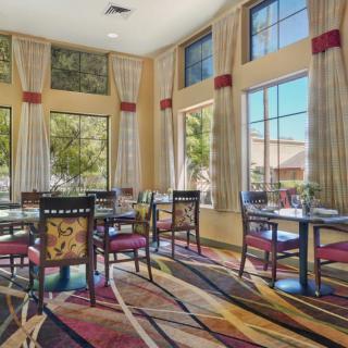 A bright and spacious dining room with multiple tables and chairs, surrounded by large windows and elegant curtains.