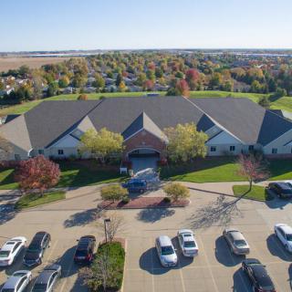 Aerial view of a suburban building with a parking lot surrounded by trees and a residential area in the background.