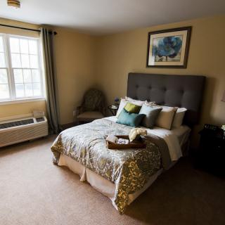 A cozy bedroom with a neatly made bed, artwork above the headboard, and a window letting in natural light.