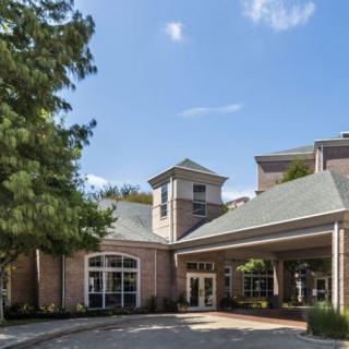 A brick building with a covered entrance and surrounding trees under a clear blue sky.