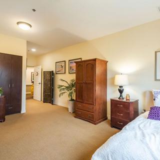 A cozy bedroom interior with furniture, including a bed, wardrobe, nightstand, and indoor plants.