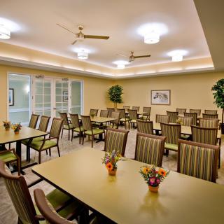 A well-lit dining room or conference space with neatly arranged chairs and tables, complemented by decorative plants.