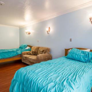 A cozy bedroom with two turquoise-covered beds and a small couch against a light blue wall.