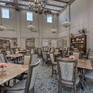 An elegant dining room with multiple tables and chairs, adorned with chandeliers and decorative elements.