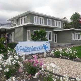 A charming house with a welcoming sign, surrounded by beautiful flowers on a cloudy day.