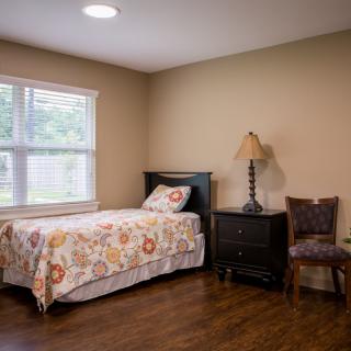 A cozy bedroom with a single bed, nightstand, and a chair by the window.