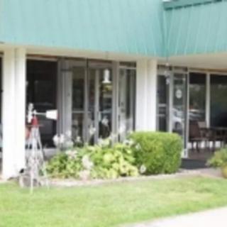 A storefront with a green roof and glass windows, surrounded by landscaping and bushes.