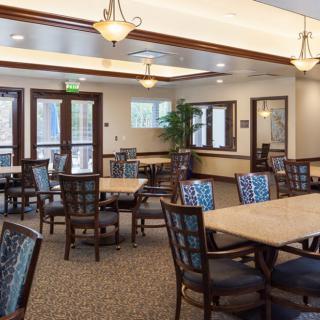 A spacious dining room with multiple tables and chairs, featuring elegant lighting and large windows.