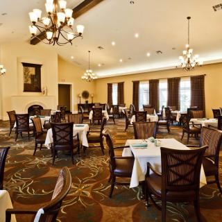 An elegant dining room with neatly arranged tables and chairs, illuminated by chandeliers.