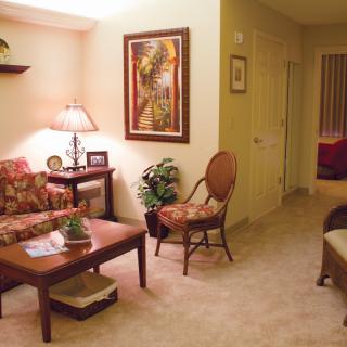 A cozy living room with a warm color palette, featuring artwork on the wall, a lamp on a side table, and comfortable seating.