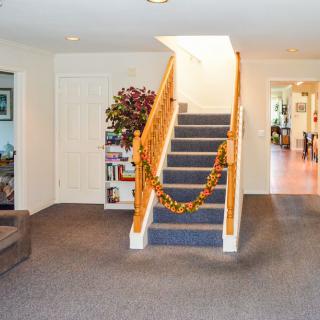 A cozy living room featuring a decorated staircase with garlands, carpeted flooring, and a bookcase next to the stairs.