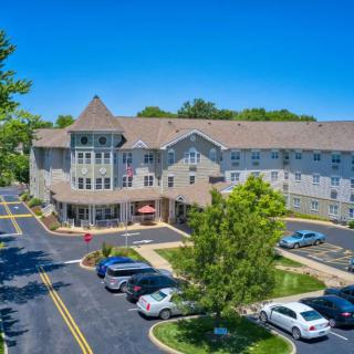 Aerial view of a multi-story residential building with a parking lot and surrounding trees under a clear blue sky.