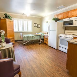 A spacious, well-lit room featuring a kitchen area and a hospital bed, designed for comfort and care.