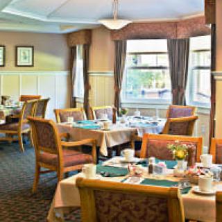 A cozy dining room with neatly arranged tables and chairs, featuring large windows with curtains.