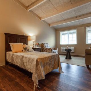 A cozy bedroom featuring a single bed, wooden floors, and ample natural light.