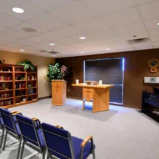 A small chapel interior with chairs, an altar, and a bookshelf.