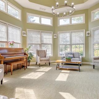 A bright living room featuring a piano, armchairs, and large windows that let in plenty of natural light.