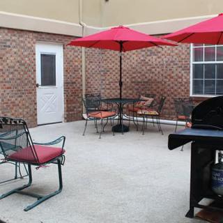 A cozy outdoor patio area with tables, chairs, and umbrellas next to a brick wall.