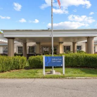 Front view of a healthcare facility with an American flag and a sign in the foreground.