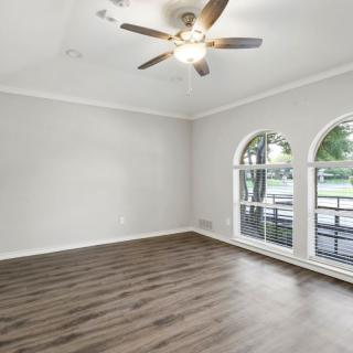 A modern living room with hardwood floors, large windows, and a ceiling fan.