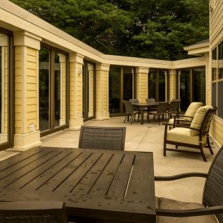 A spacious patio featuring outdoor furniture and surrounded by glass doors, with trees in the background.