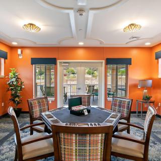 A brightly colored dining room with an orange theme, featuring a central round table and chairs, surrounded by windows and decorated with indoor plants.